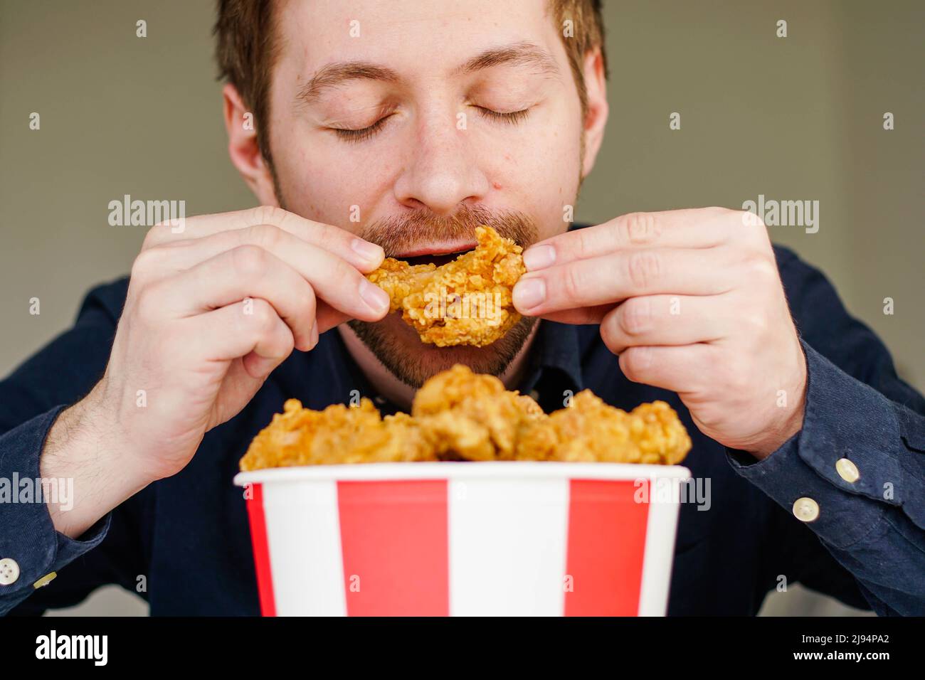 Hungry excited guy eating fried chicken wings. Caucasian man enjoying junk food. Stock Photo