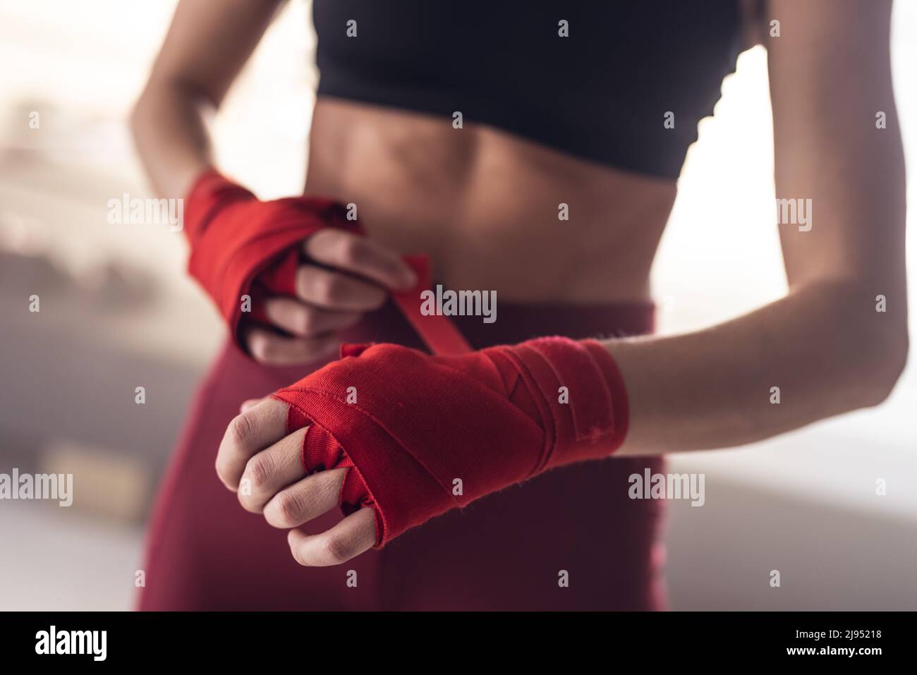Midsection of caucasian young female boxer wrapping hands with red boxing wraps in health club Stock Photo
