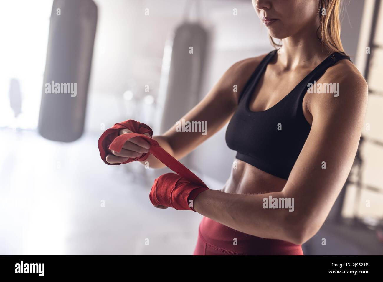 Midsection of caucasian young female boxer wrapping hands with red boxing wrap at health club Stock Photo