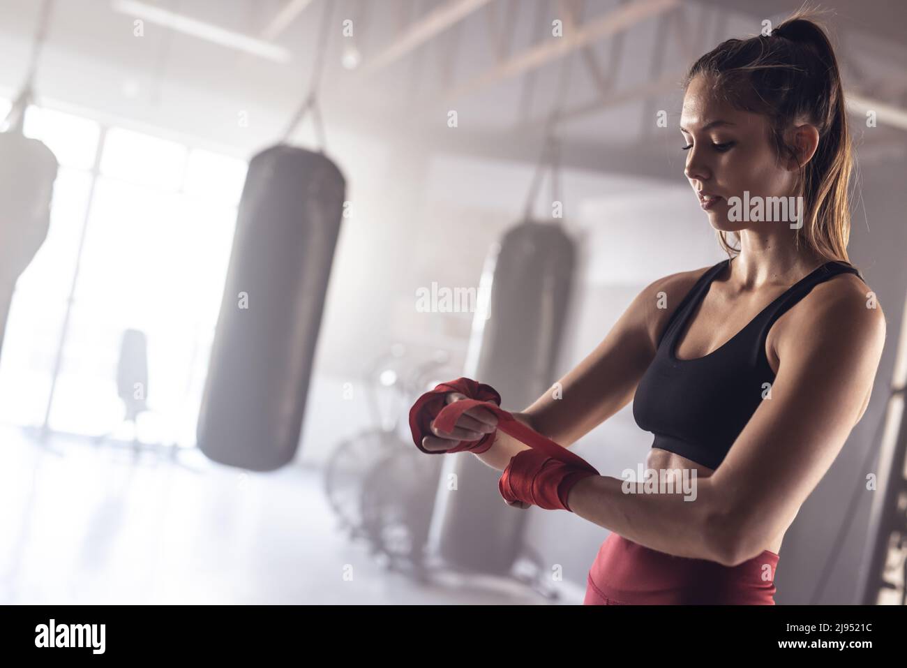Confident caucasian young female boxer wrapping hands with red boxing wraps in health club Stock Photo