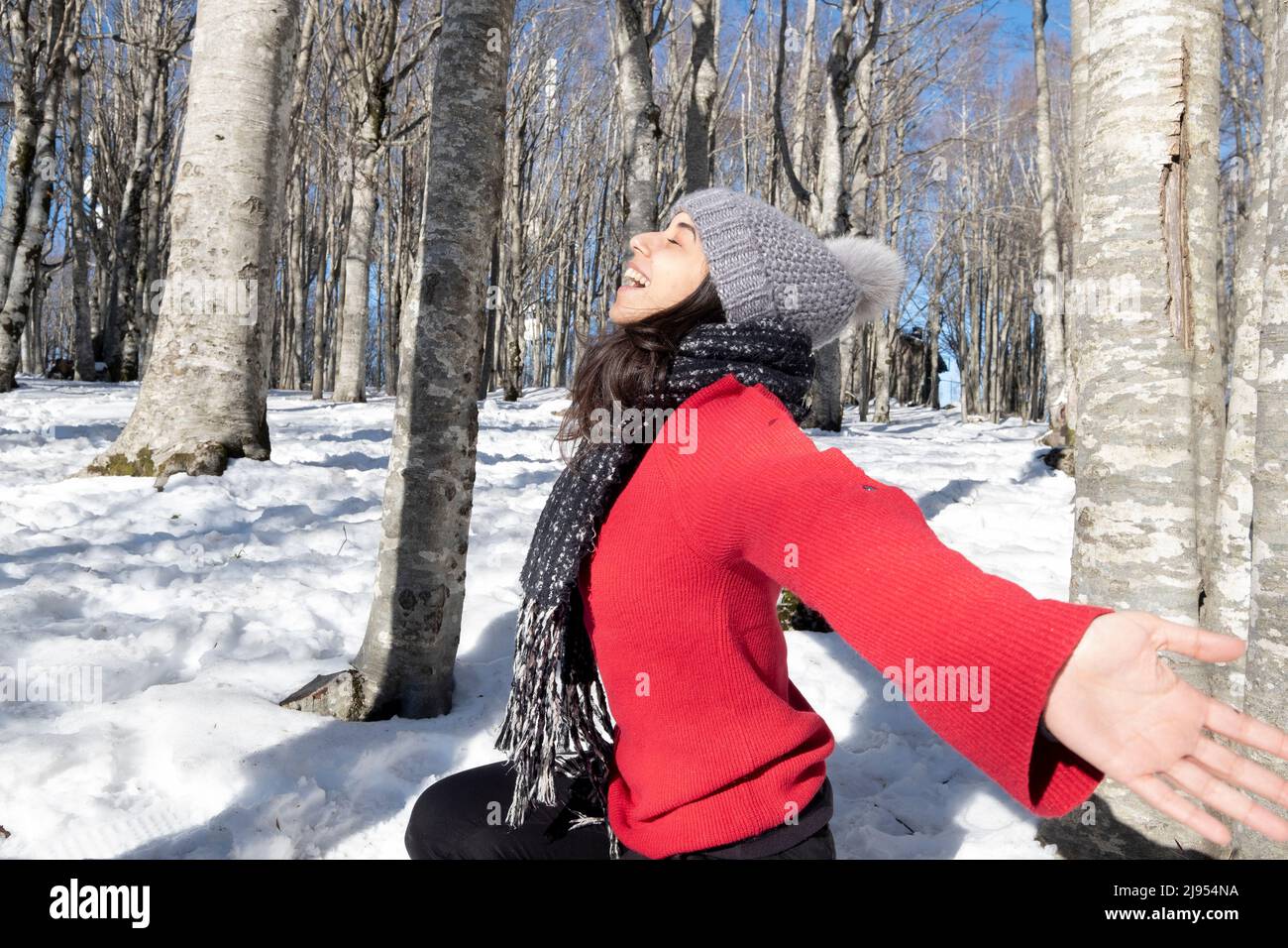 Brunette woman in winter forest. Outdoor portrait of young woman in winter cap and muffler enjoying the winter. Posing and having fun. Italy Stock Photo