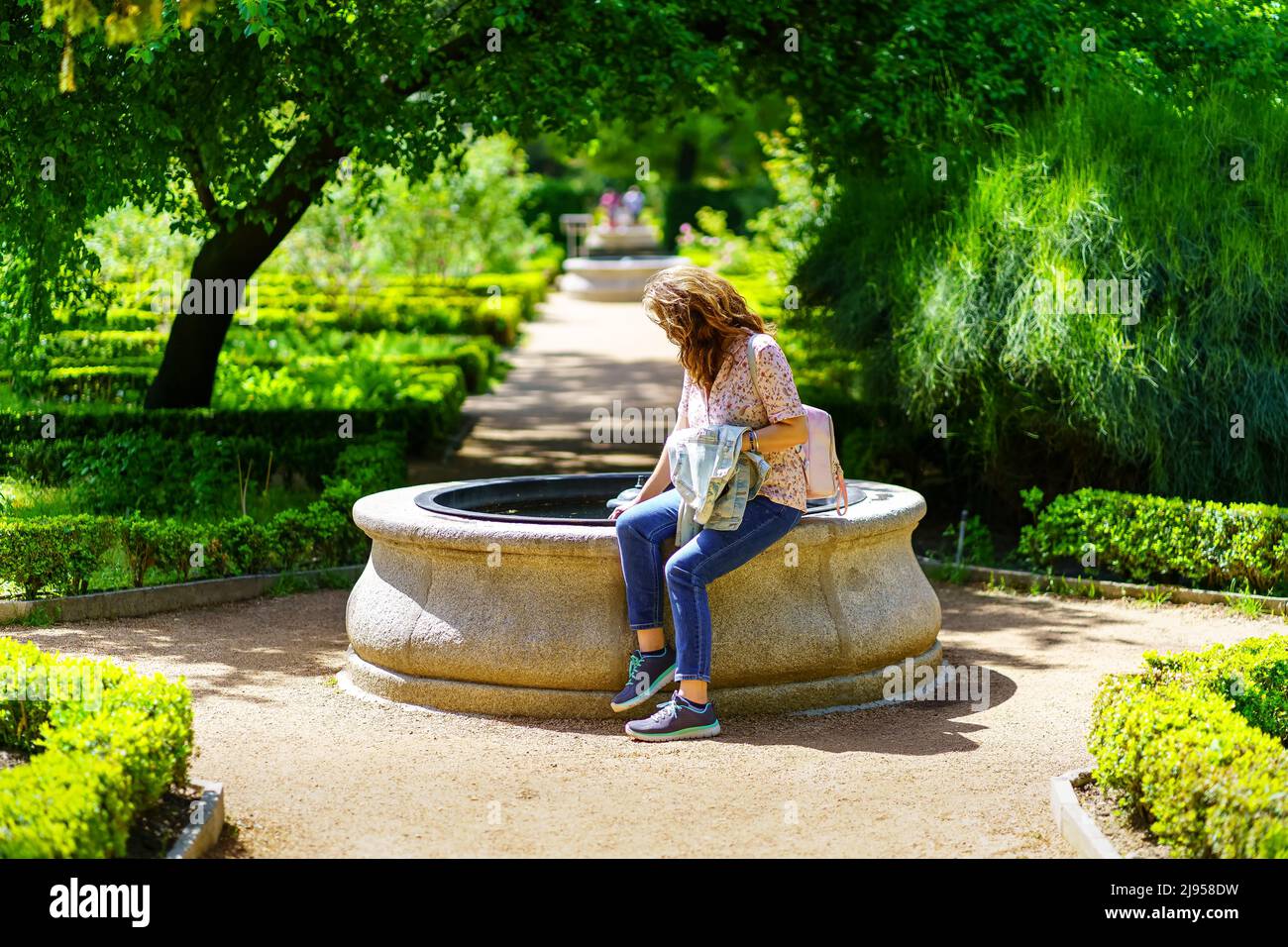 Woman sitting in a small fountain of fresh water in the center of the garden. Stock Photo