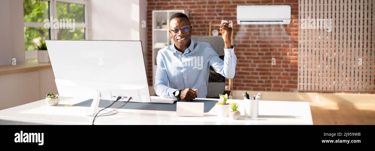 Young Businessman Operating Air Conditioner With Remote Controller In Office Stock Photo