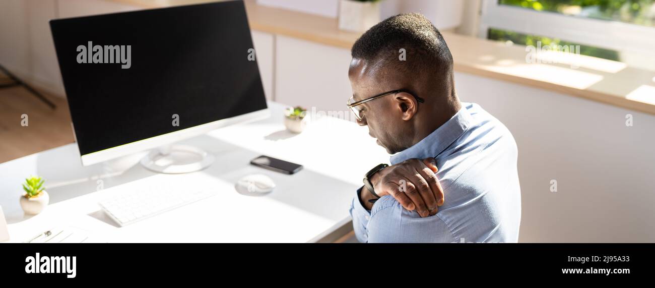 Businessman Suffering From Shoulder Pain While Working In Office Stock Photo