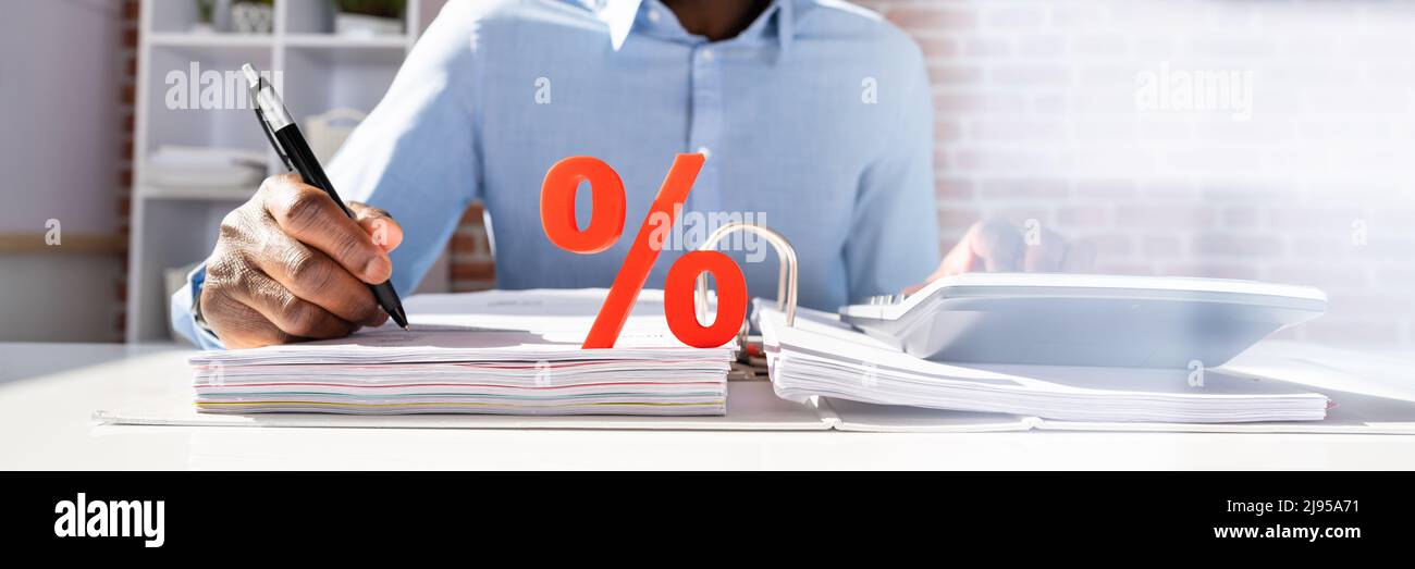 Close-up Of White Block With Percentage Symbol While Businessperson Calculating Invoice Over White Desk Stock Photo