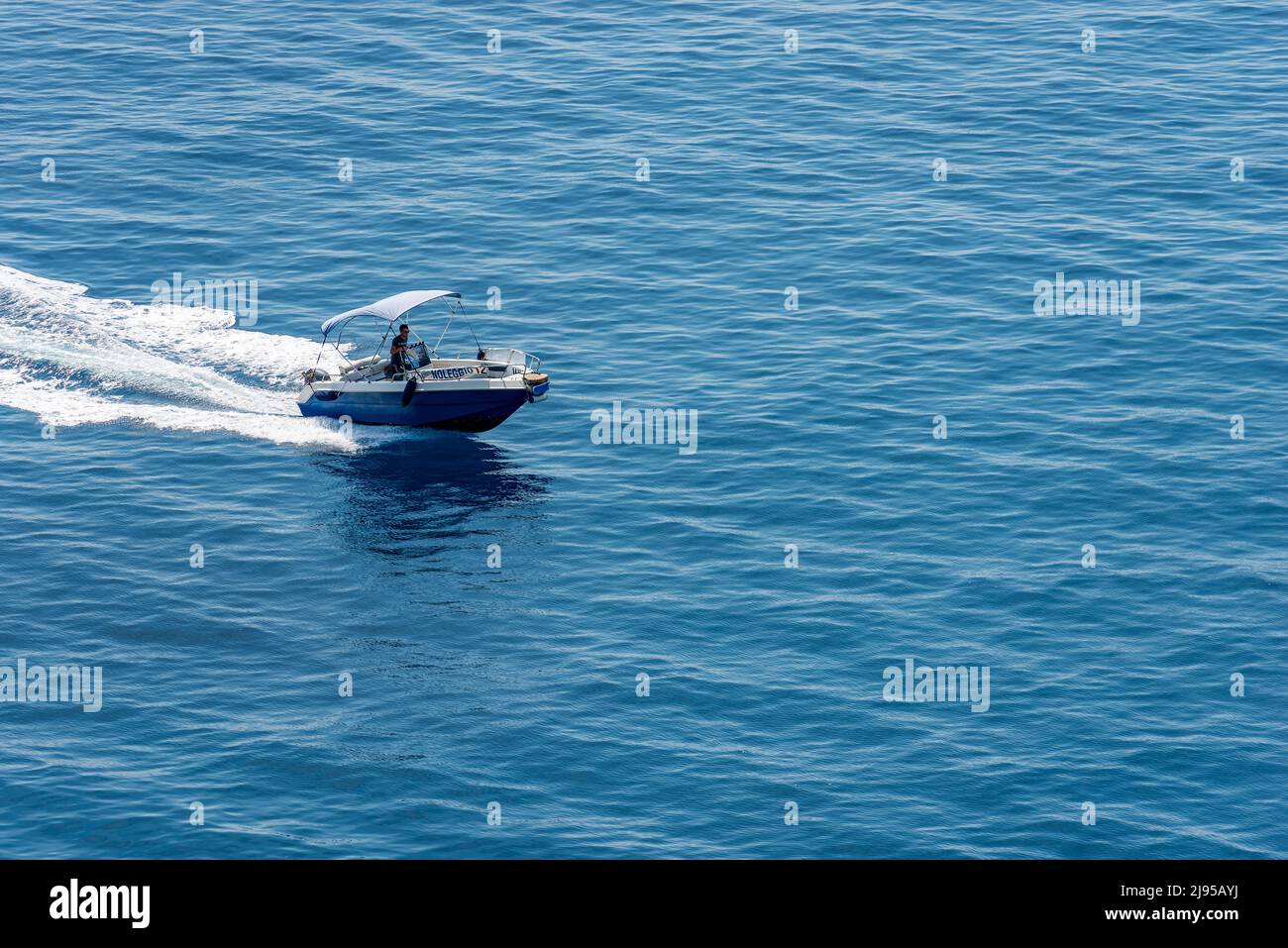 Small blue motor boat with one person on board runs fast in the blue Mediterranean sea with white wake, Cinque Terre, Liguria, Italy. Stock Photo