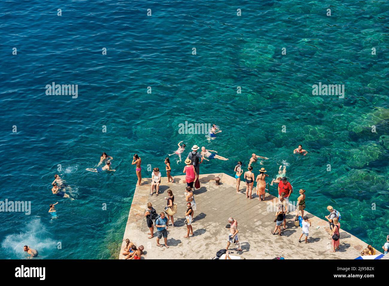 Group of people swim and sunbathe in the sea of the small village of Vernazza, Cinque Terre, UNESCO world heritage site. La Spezia, Liguria, Italy. Stock Photo