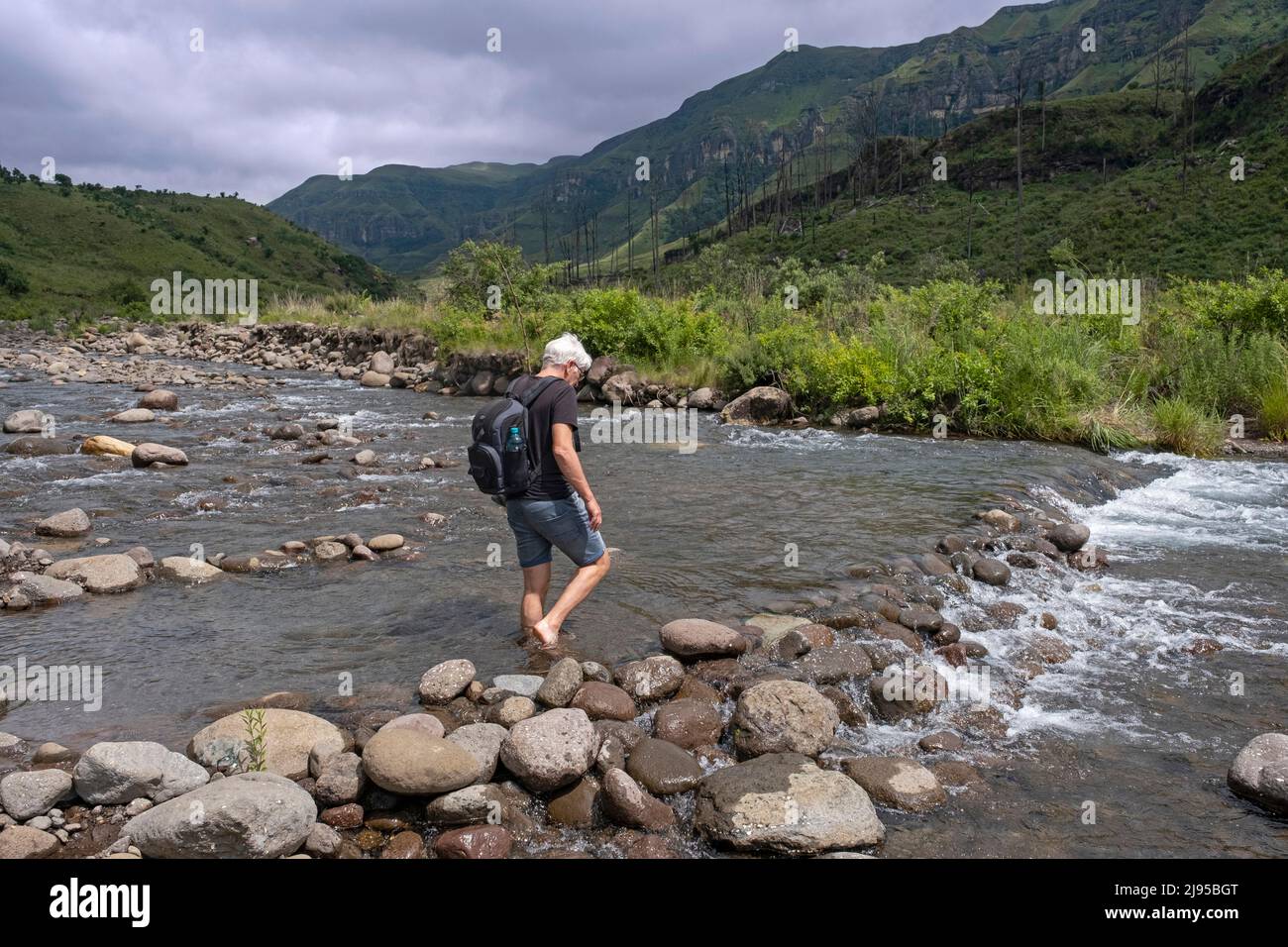 Drakensberg Mountain Range and Western tourist crossing stream in the Injisuthi area in KwaZulu-Natal, South Africa Stock Photo