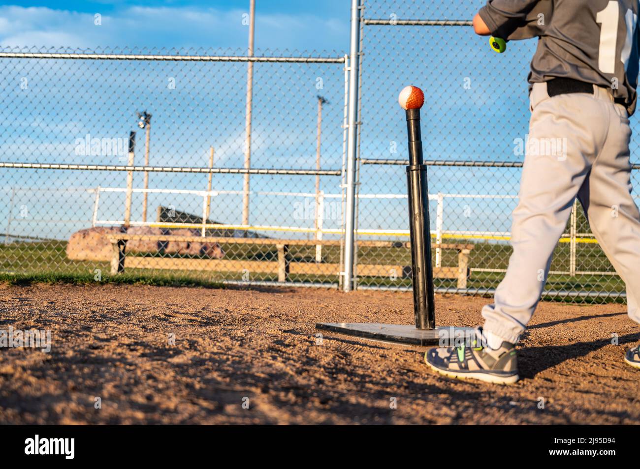 Youth baseball player standing at home plate to hit a ball off a tee with a bat. Stock Photo