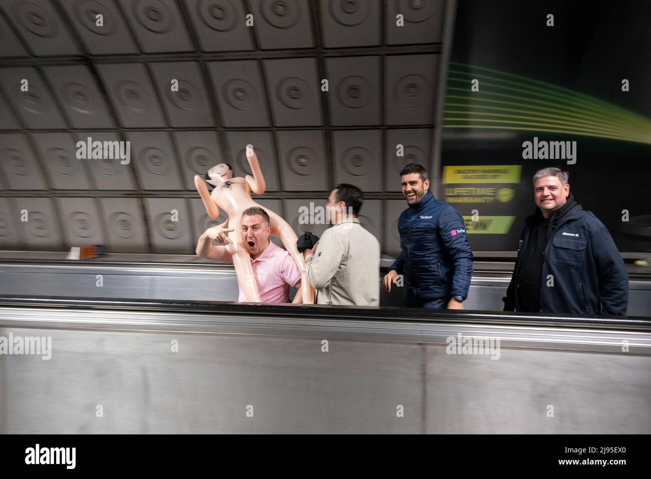 Group of men most likely on a stag party or stag do, travel along the moving walkway at Waterloo station carring a male blow up doll on 30th April 2022 in London, United Kingdom. A bachelor party, also known as a stag weekend, stag do or stag party, or a bucks night is a party held/arranged by the man who is shortly to enter marriage. Stock Photo