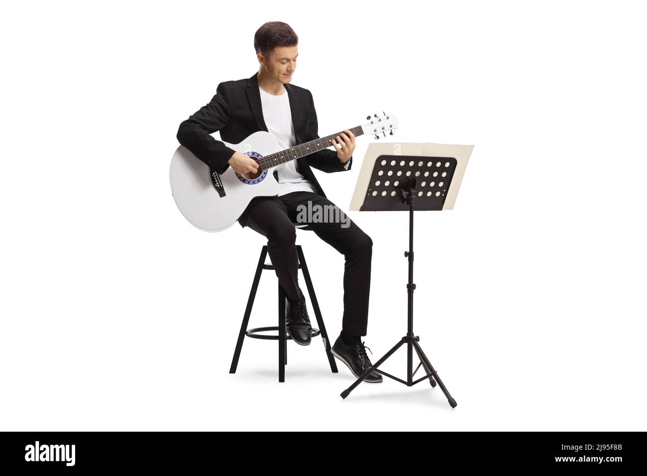 Young man in a black suit sitting on a chair and playing an acoustic ...