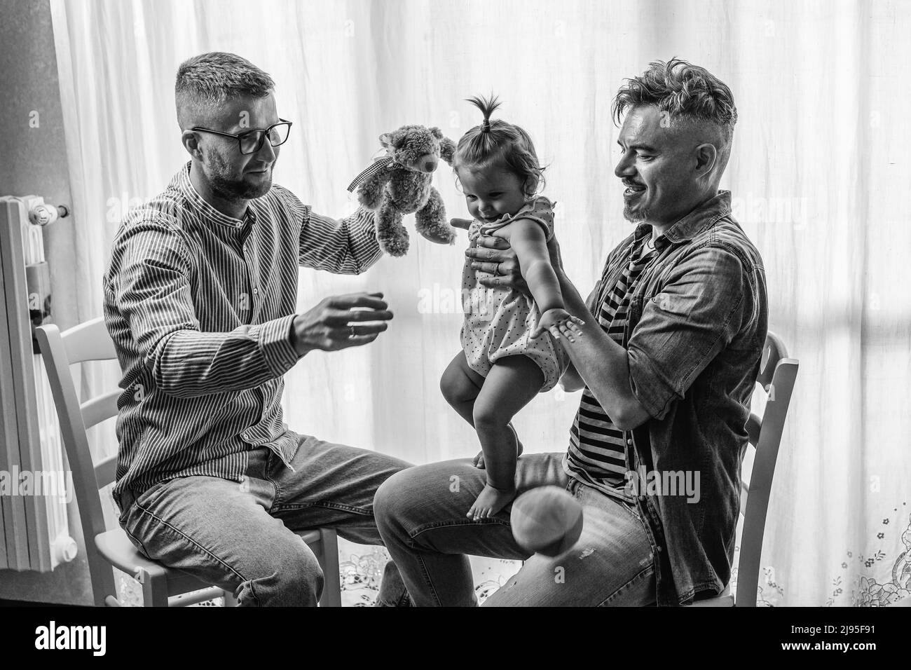 Male gay couple with adopted baby girl at home - Two handsome fathers playing with their daughter - Lgbtq+ family at home - Diversity concept and LGBT Stock Photo