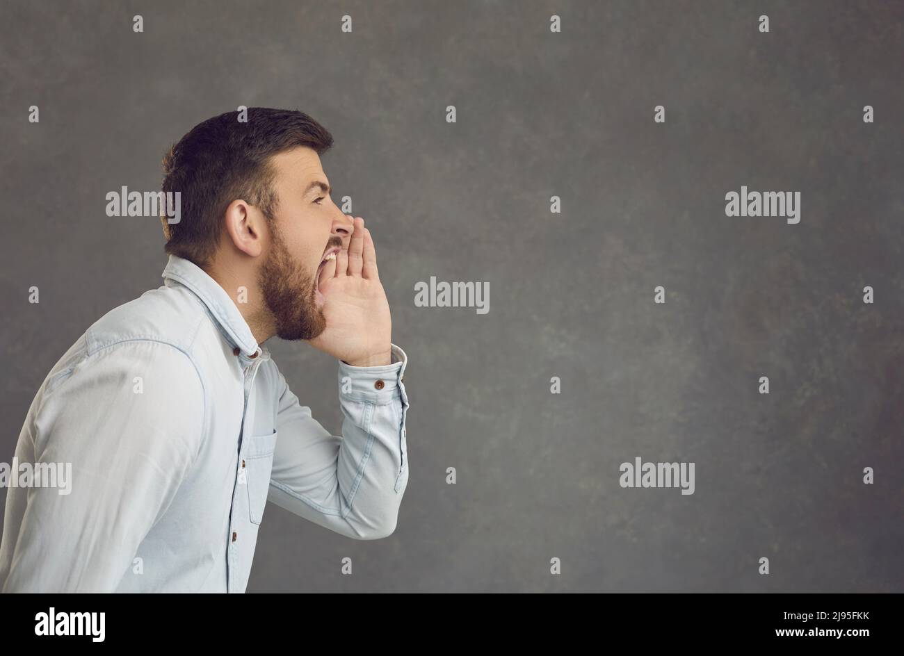 Side profile portrait of a man on a gray background who shouts announcing promotional information. Stock Photo