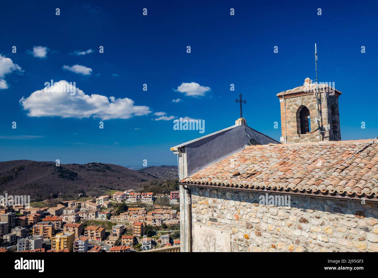 The small village of Tolfa, in Lazio. The Sanctuary of the Madonna della Rocca on top of the cliff. The inhabited center and the roofs of the houses s Stock Photo