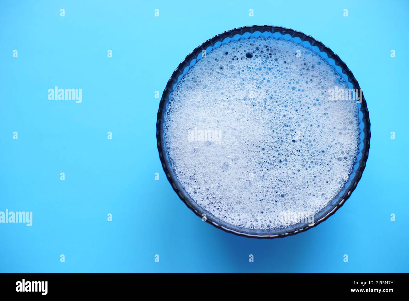 Glass bowl with foam water and bubbles on a blue table, copy space. Stock Photo