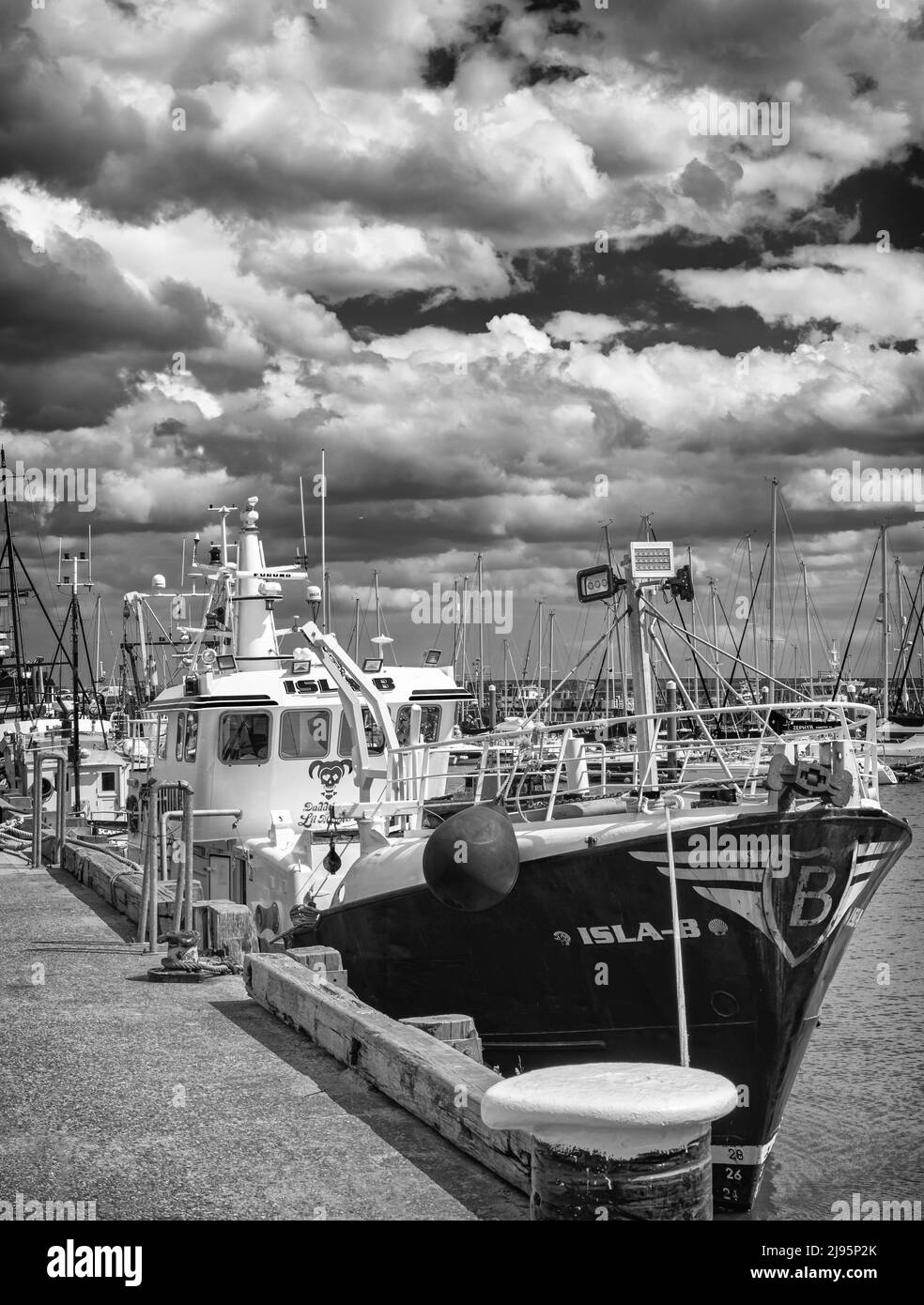 A trawler is moored at a quay. Ropes make the boat fast and the bridge bristles with antenae. A cloudy sky is above. Stock Photo