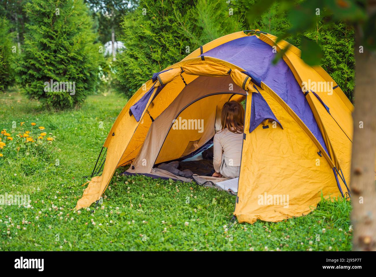 Small children, kids play, read in orange tourist tent. Family trip, hike to nature. Backyard games, having fun. Outdoor recreation, activity. Self-as Stock Photo