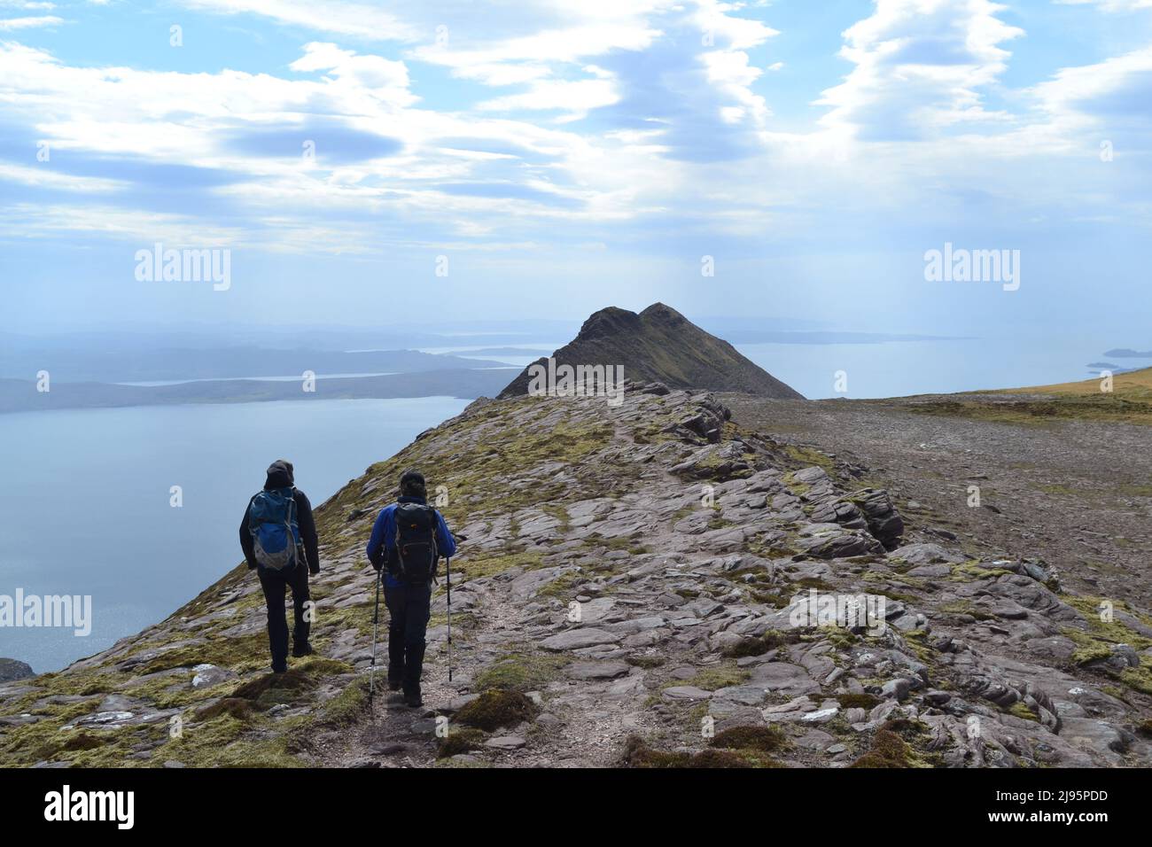 Hikers/hill walkers in silhouette on Ben Mor Coigach, a ridge near Ullapool, north west Scotland, Assynt, admire views of Summer Isles on a spring day Stock Photo