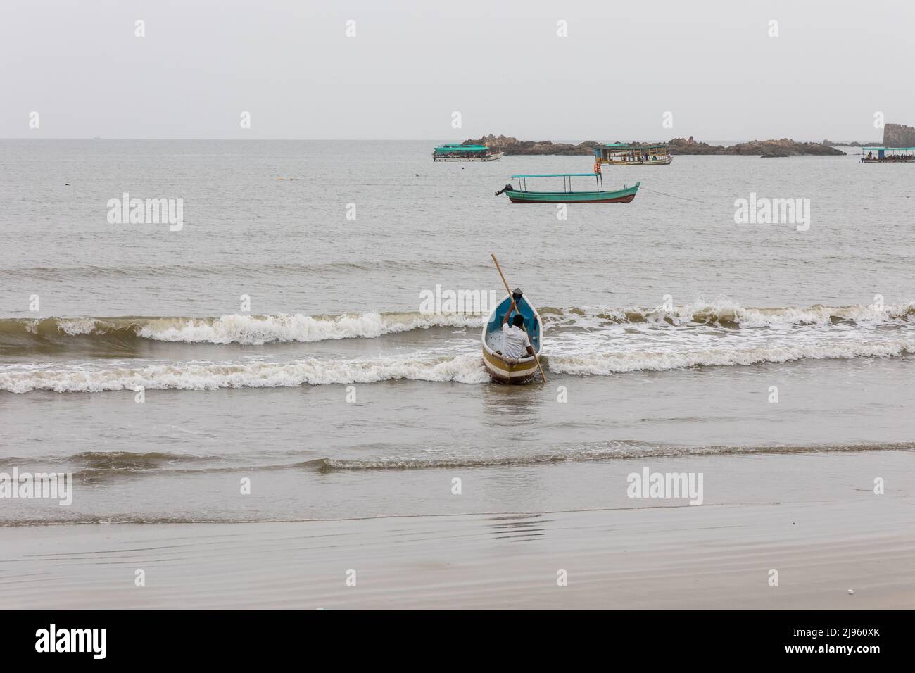 Fisherman venturing into sea on his canoe on an overcast day in Malvan, Maharashtra Stock Photo