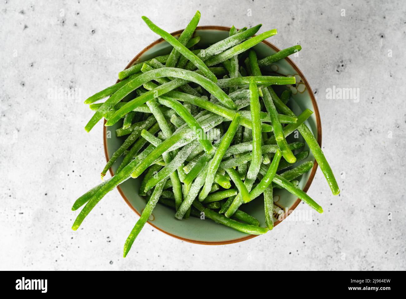 Frozen green beans, haricots verts, close up in a bowl on light grey