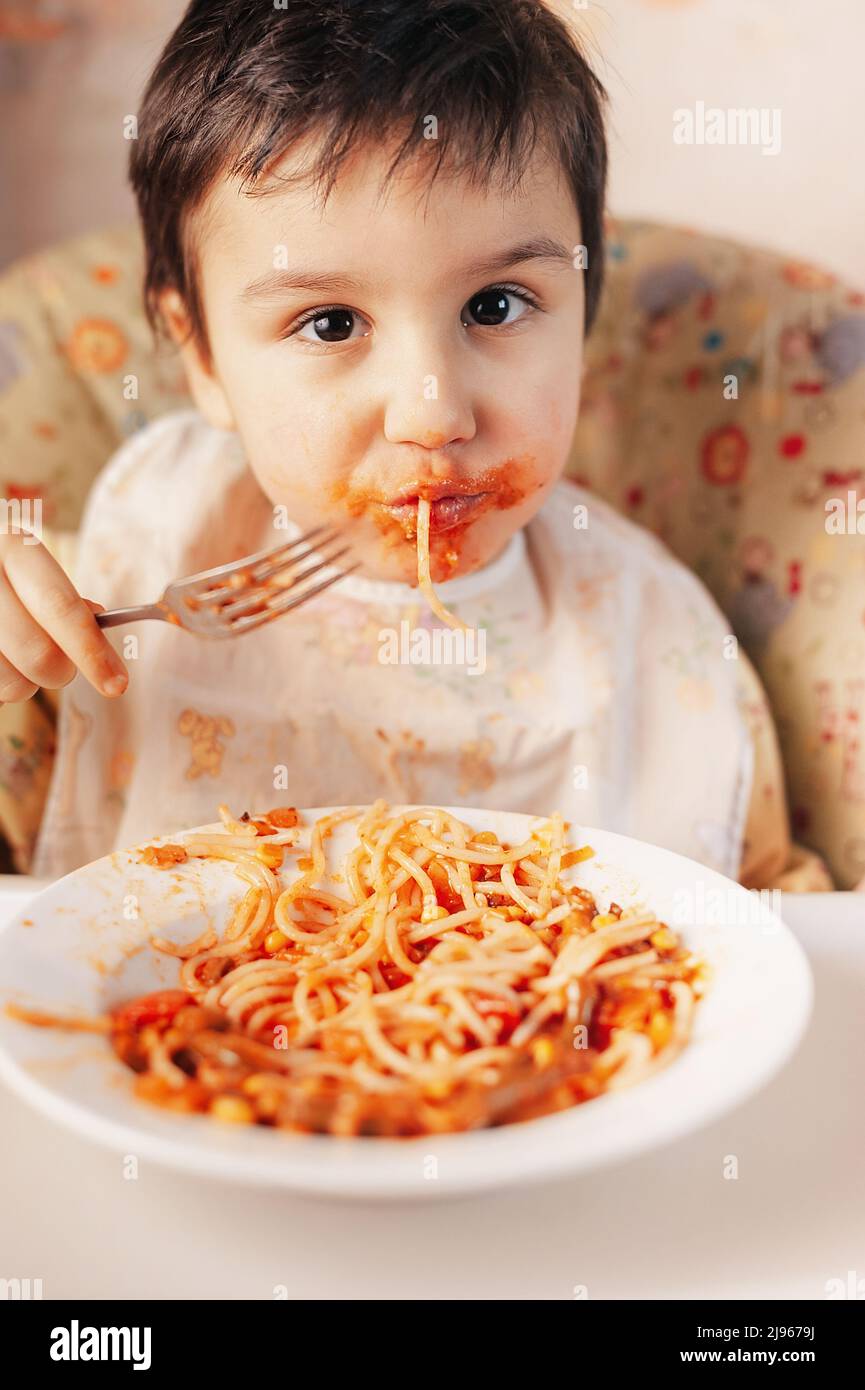 Child eating spaghetti with vegetables. Kid having fun eating. Brown
