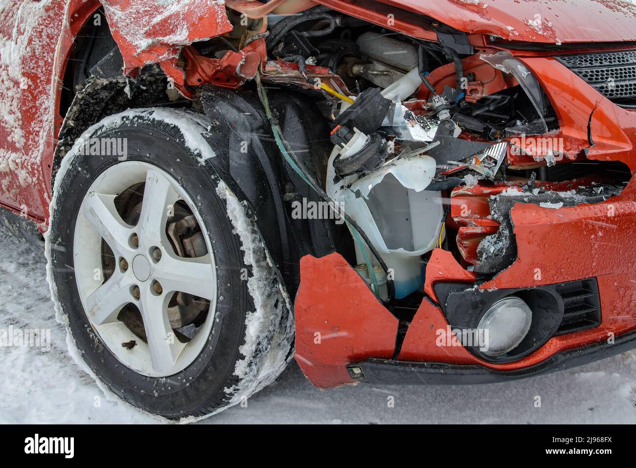 Front corner of an unidentified smashed car. Most of the fender is missing. Broken plastic and metal visible in the hole. Snow on ground and tire. Stock Photo