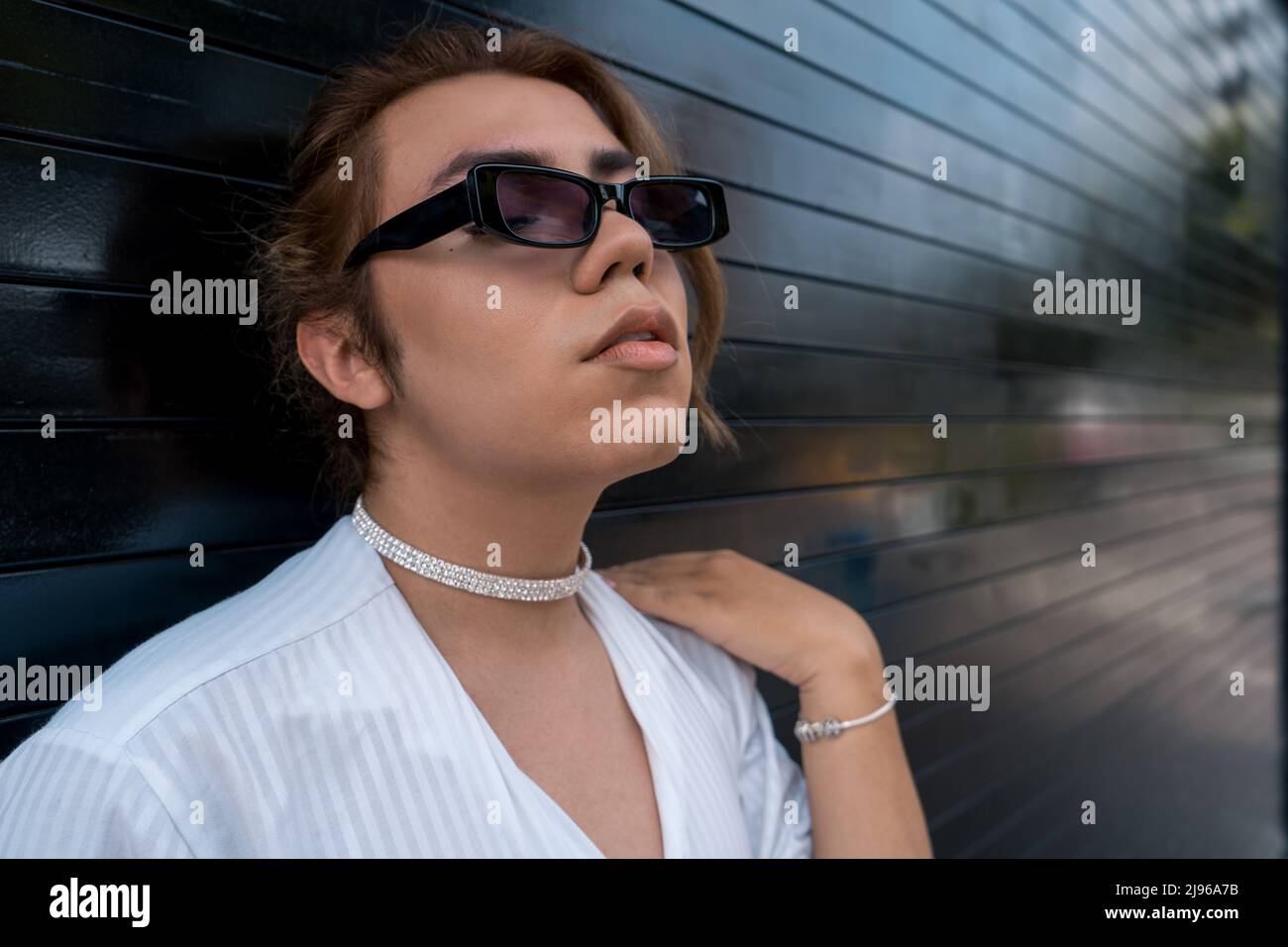 non binary man with sunglasses leaning on black gate in the street remembering Stock Photo