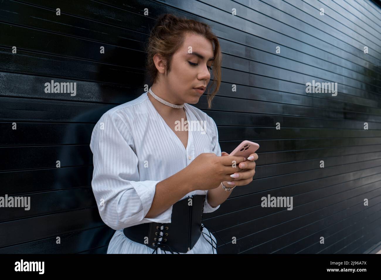 non-binary using phone in her hands chating leaning on black gate in the street remembering Stock Photo