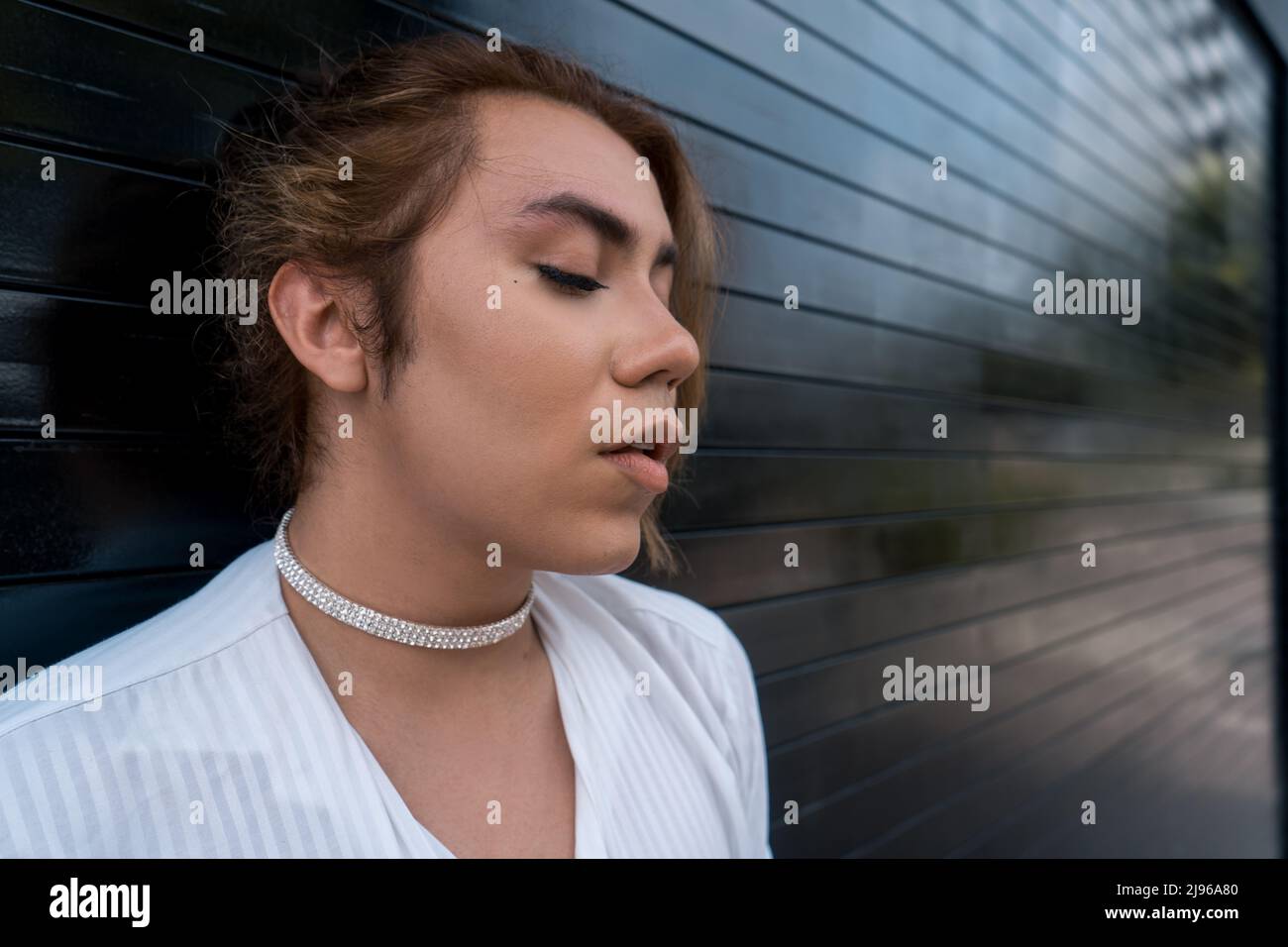 non-binary using phone in her hands chating leaning on black gate in the street remembering Stock Photo
