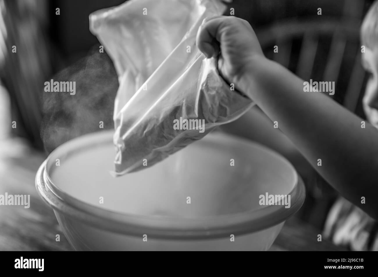Little child dumping ingredients into a bowl causing dust to rise into the air. Stock Photo