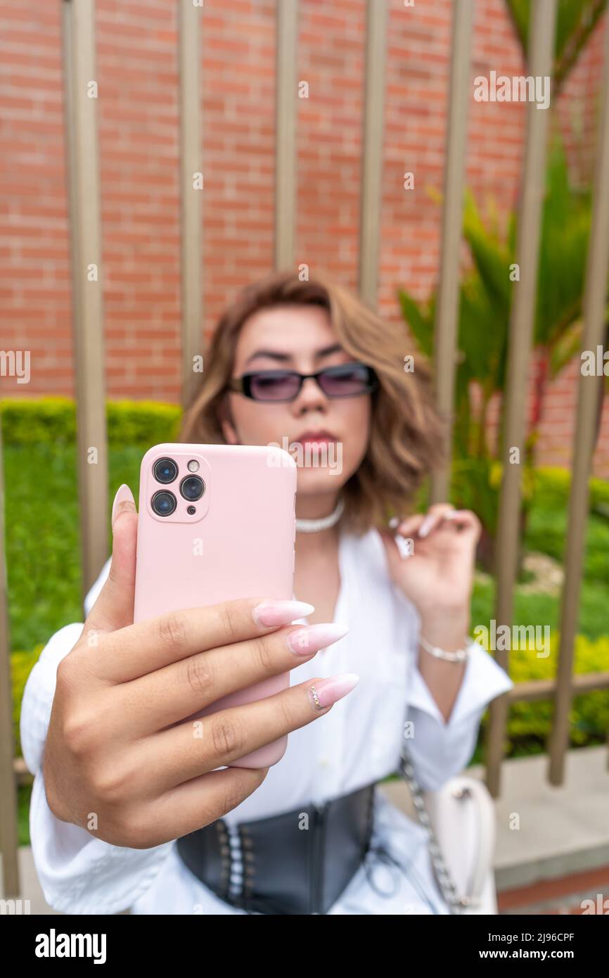 nonbinary vain man taking selfie leaning on black gate in the street