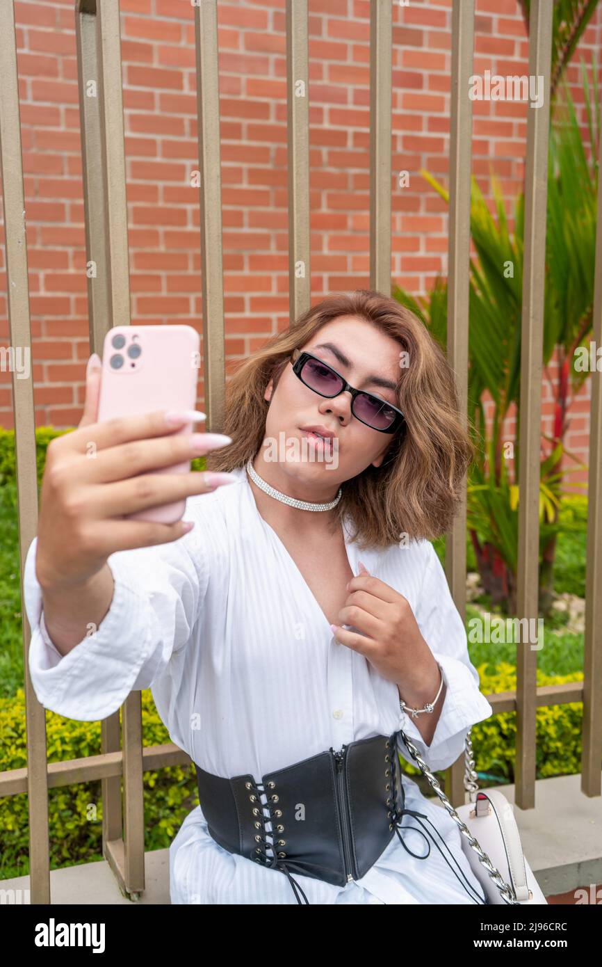 nonbinary vain man taking selfie leaning on black gate in the street