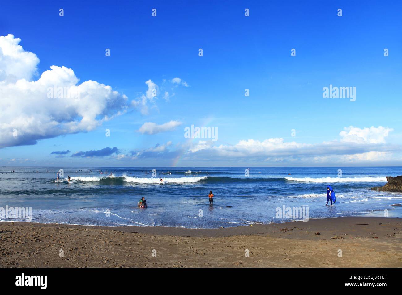 Surfers Riding Waves with a Rainbow on the horizon at Batu Bolong Beach in Canggu, Bali, Indonesia Stock Photo