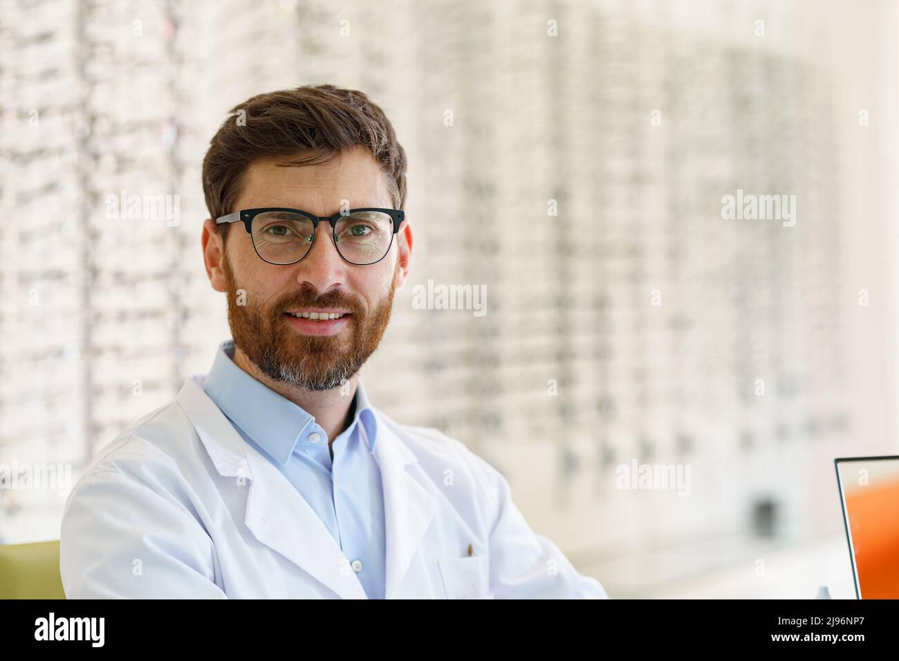 Handsome smiling ophthalmologist in front of the showcase with eyeglasses in the optical store Stock Photo