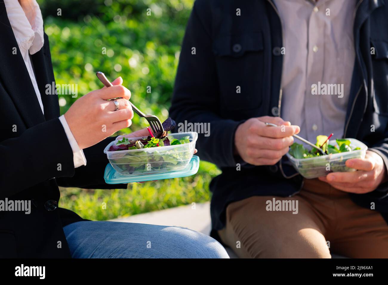 hands of two people eating a salad in a park Stock Photo