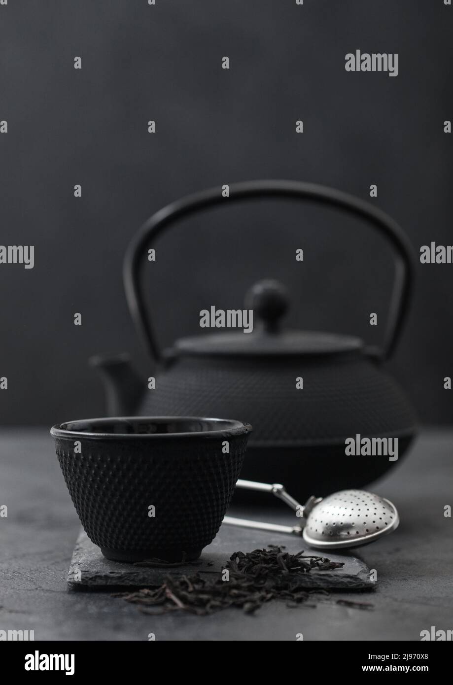 Chinese teapot with infuser and cup with loose black tea on black Stock