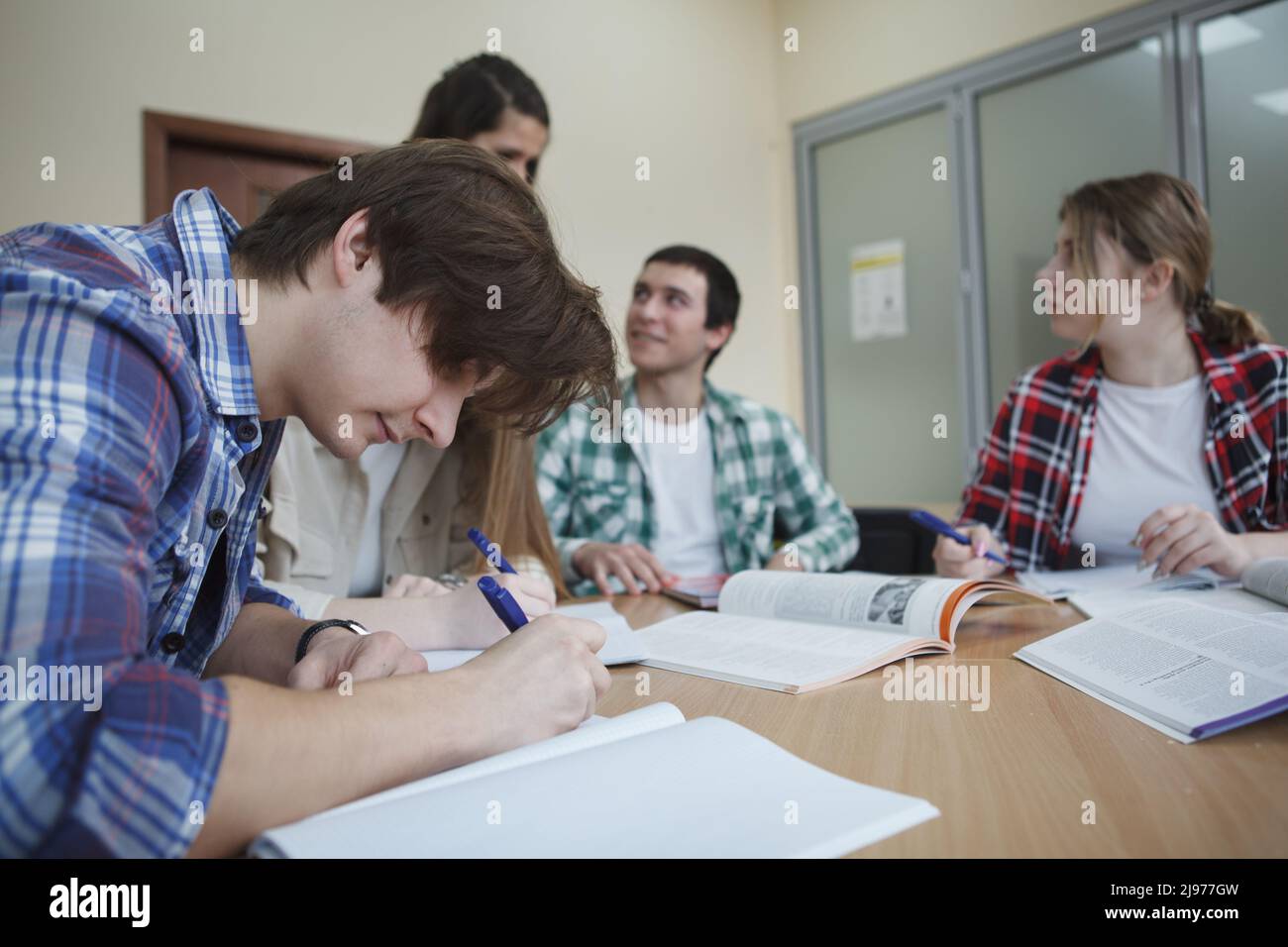 Young man writing notes during class, his classmates talking on background Stock Photo