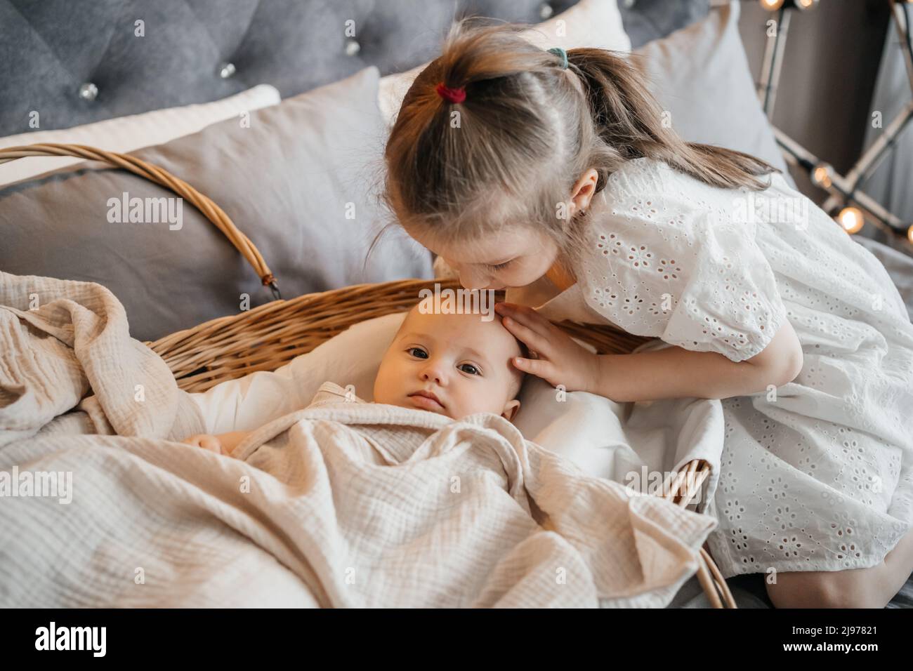 girl taking care of her younger sister on the bed wicker basket pats on
