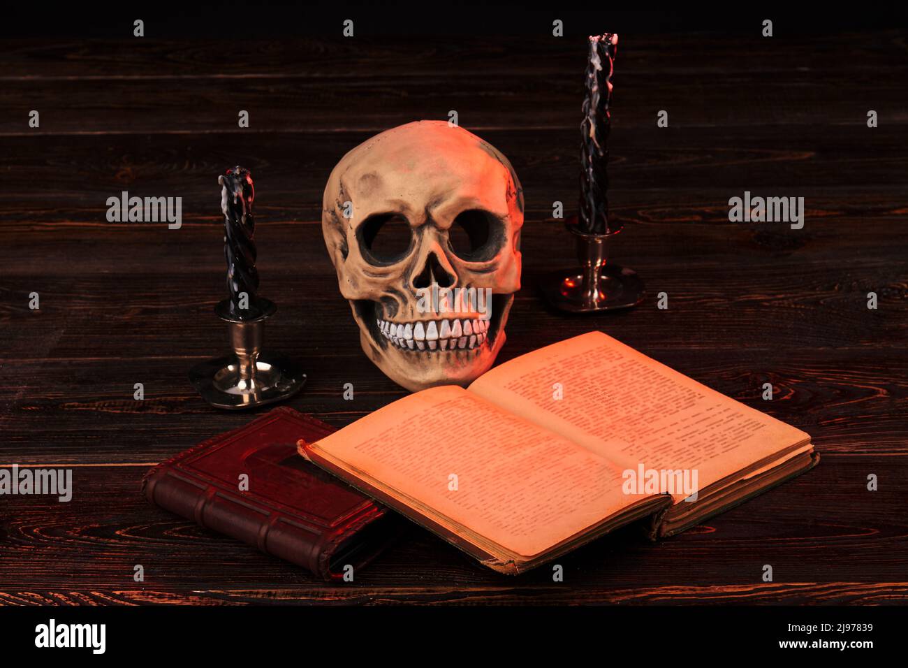 Satanism religion concept. Human skull with extinguished candles. Opened satanic bible. Stock Photo