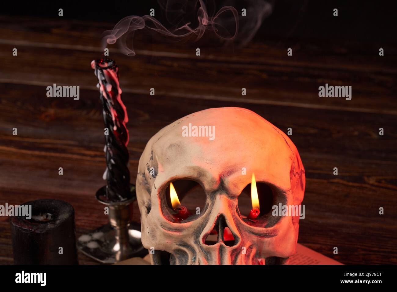 Humans skull with flame in its eyes and extinguished candles with smoke. Satanic ritual and wicca religion concept. Stock Photo