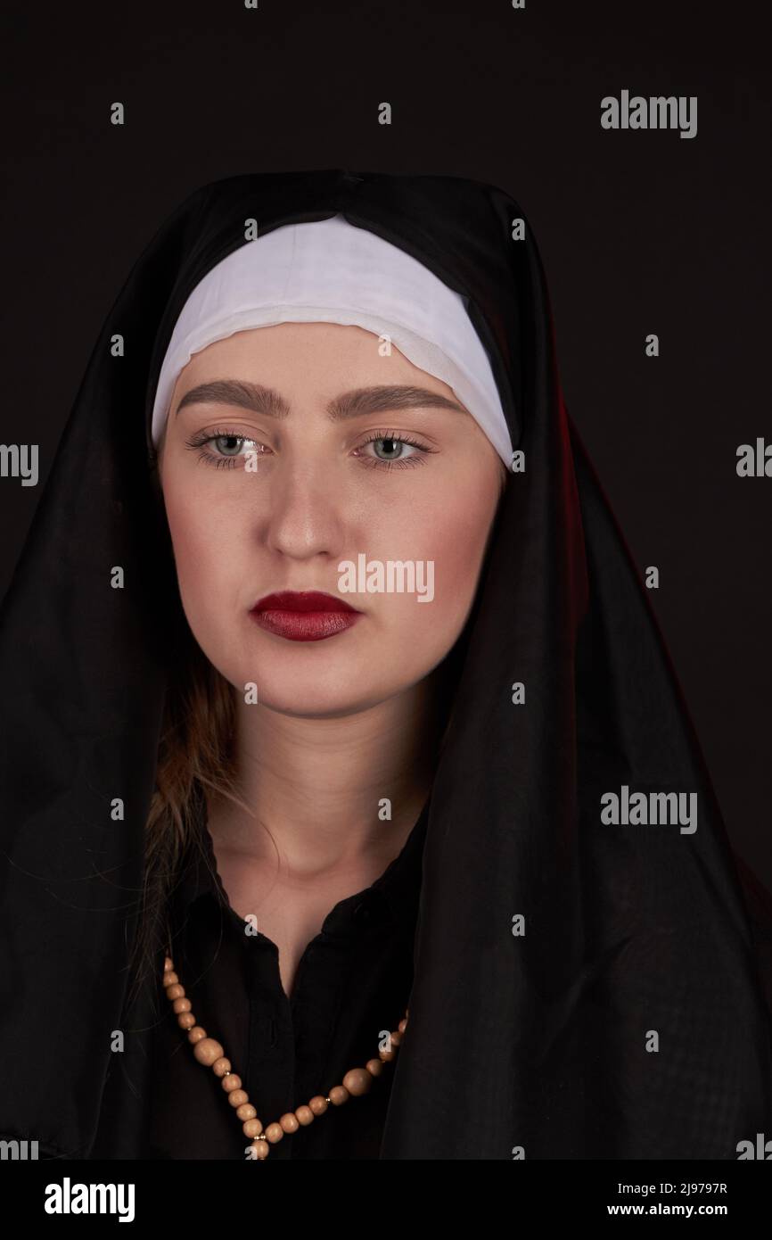 Vertical shot portrait of young nun on black background. Look with no emotions. Stock Photo