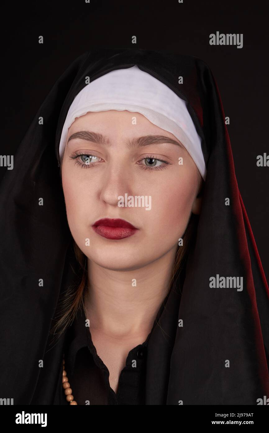 Close-up portrait of a young caucasian nun looks forward. Isolated on black background. Stock Photo