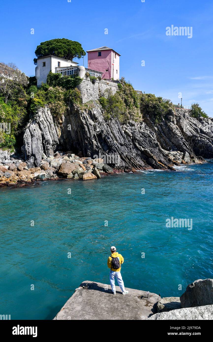 A young man rod fishing on the sea shore of the old fishing village in front of the cliff of the Anita Garibaldi Promenade, Nervi, Genoa, Liguria Stock Photo