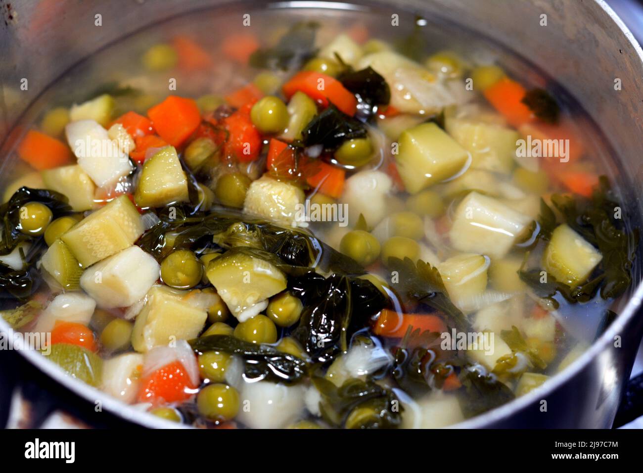 vegetables soup made of pieces and slices of carrots, peas, potatoes, onions, zucchini, celery and other fresh vegan food salted and boiled, healthy f Stock Photo