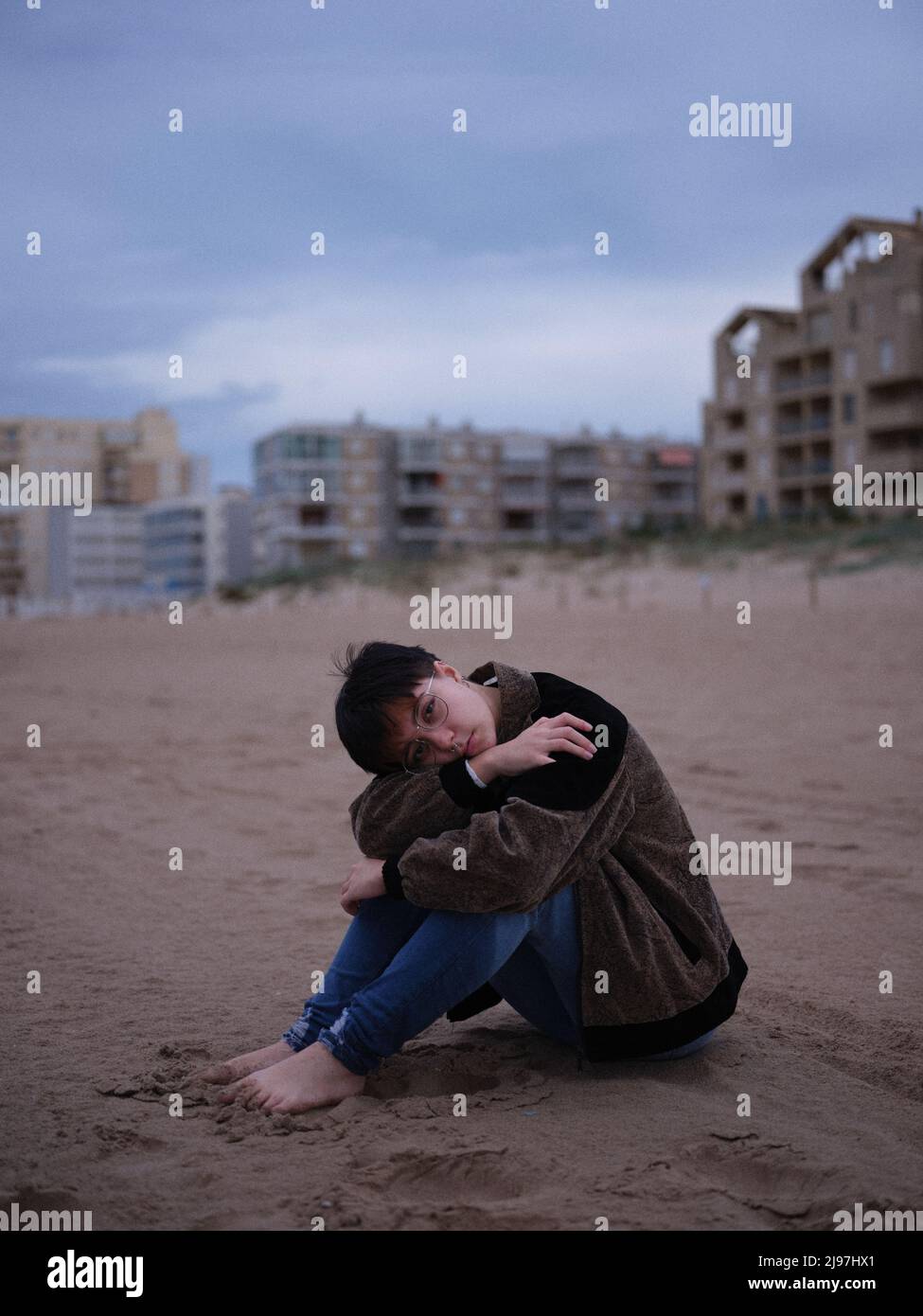 non binary young woman alone on the beach sitting on the sand Stock Photo