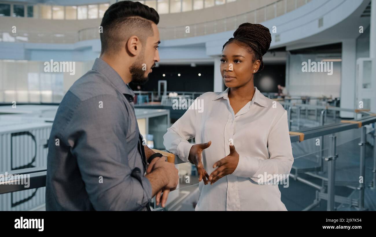 African American woman and Arabian Indian businessman talking in loft office hall working break diverse colleagues discussing news project in casual Stock Photo