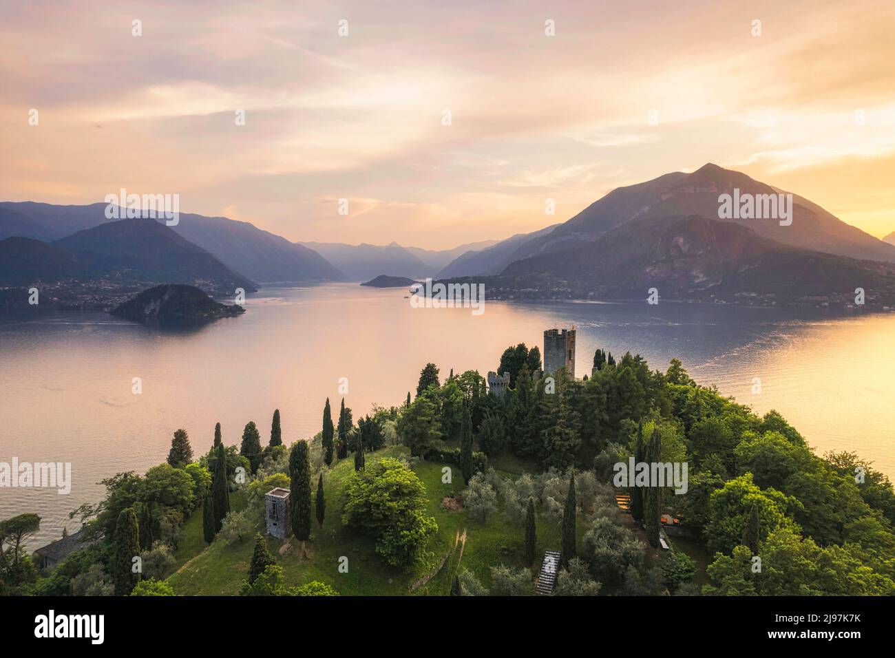 Vertical panoramic aerial view of Vezio Castle with Varenna village and mountains in background during summer sunset. Drone shot in Como lake. Varenna Stock Photo