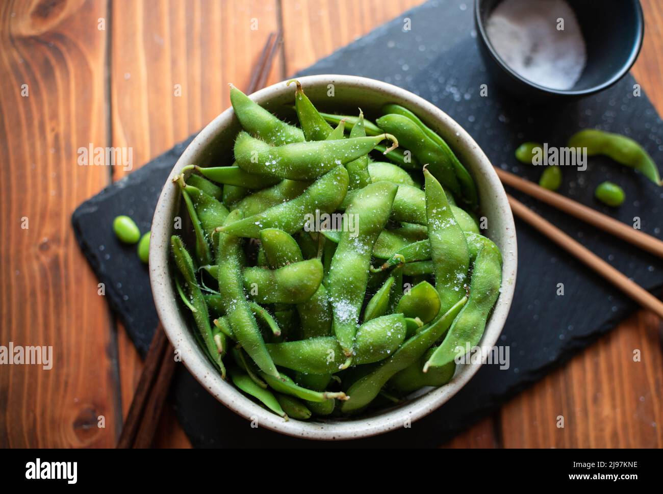 Steamed edamame sprinkled with sea salt on a dark stone board, top view