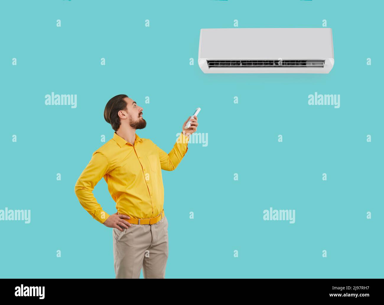 Happy man holding remote control controls or adjusts newly installed wall-mounted air conditioner. Stock Photo