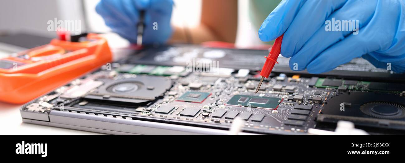 Laptop repair, hands hold voltage meter for electronics Stock Photo